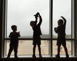 Finanzwissen altersgerecht vermitteln: Drei Kinder vor Fensterscheibe am Flughafen