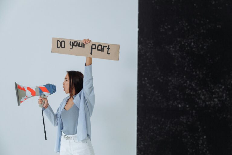 Frau hält ein Megaphon in der Hand und ein Pappschild mit der Aufforderung "Do your part".